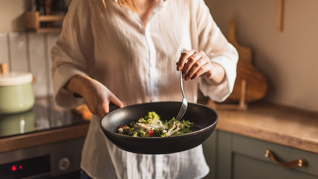 woman mid section cooking veggies in a pan