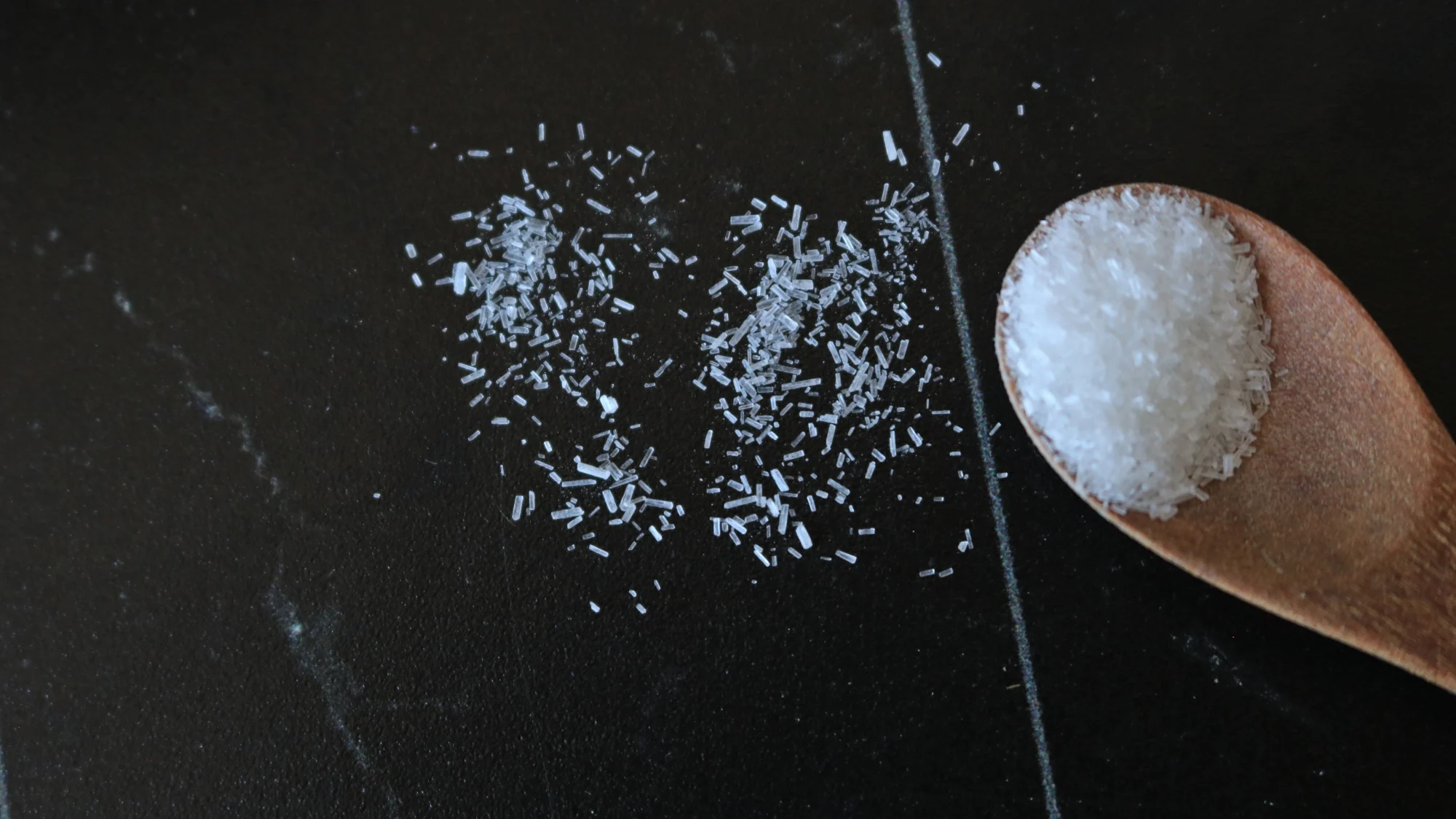 A close-up shot of MSG crystals on a black surface.