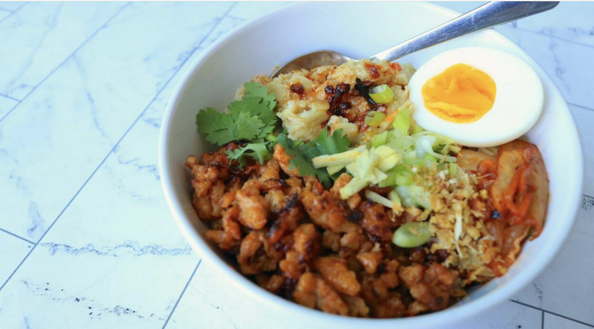 A bowl of oatmeal with ground meat, herbs, ginger, kimchi and a half of a boiled egg.