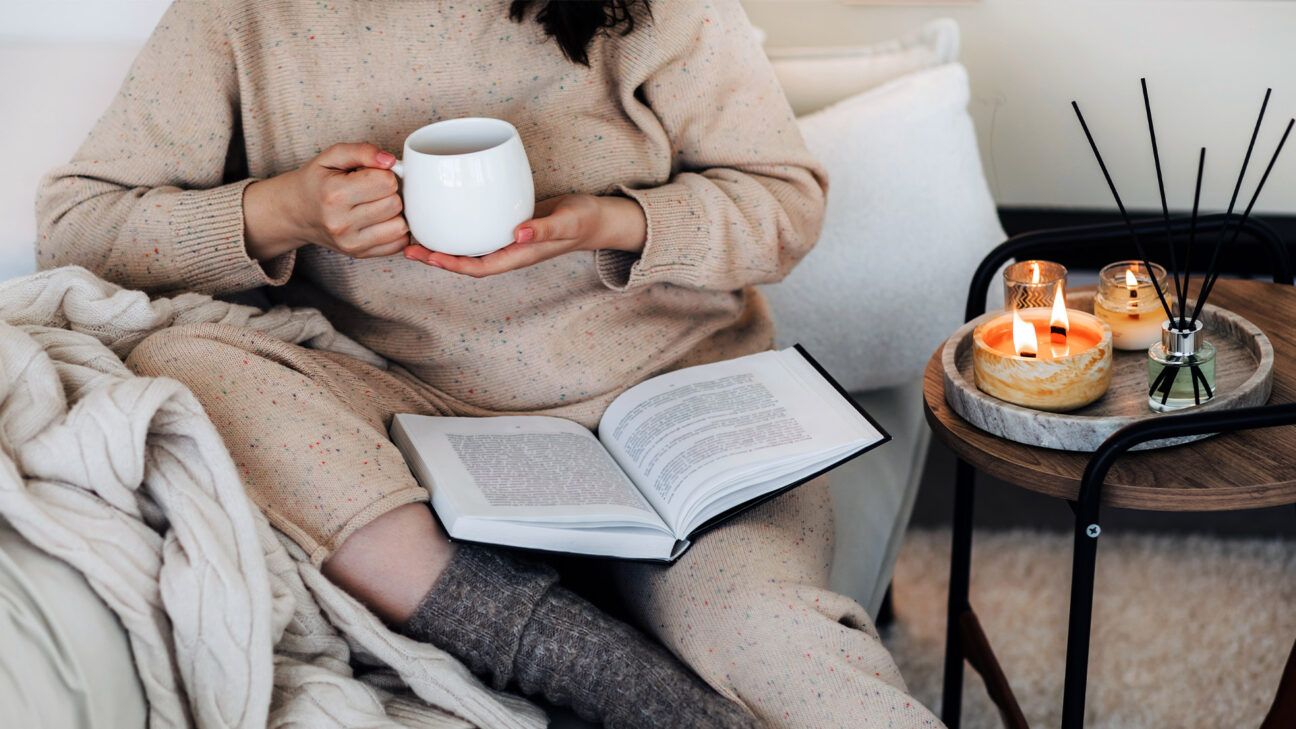 Female on couch wearing sweatpants with candles and tea