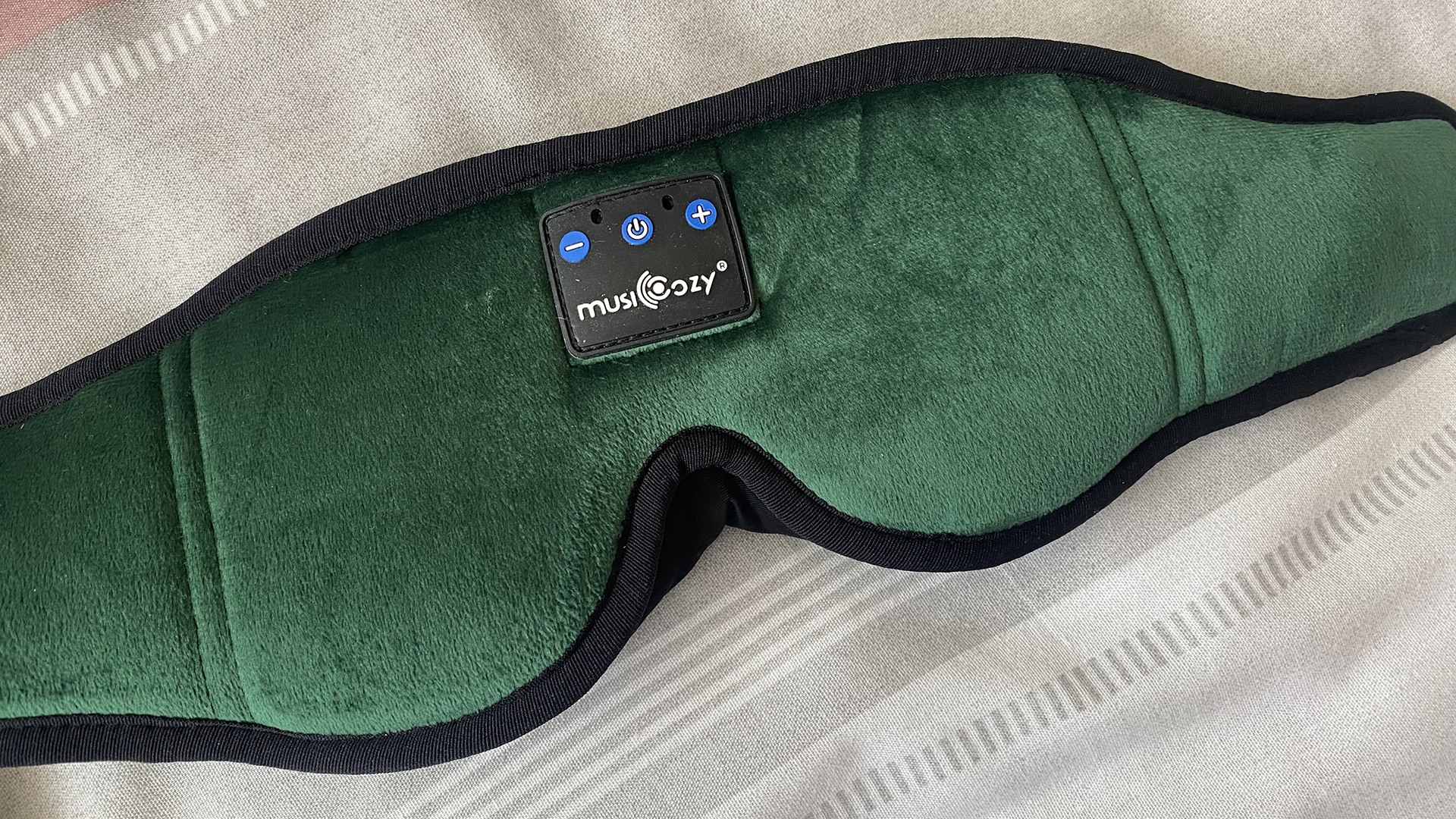A closeup of the front of the MUSICOZY Headphone Sleep Mask in green. Apart from the control panel, it looks like any other eye mask