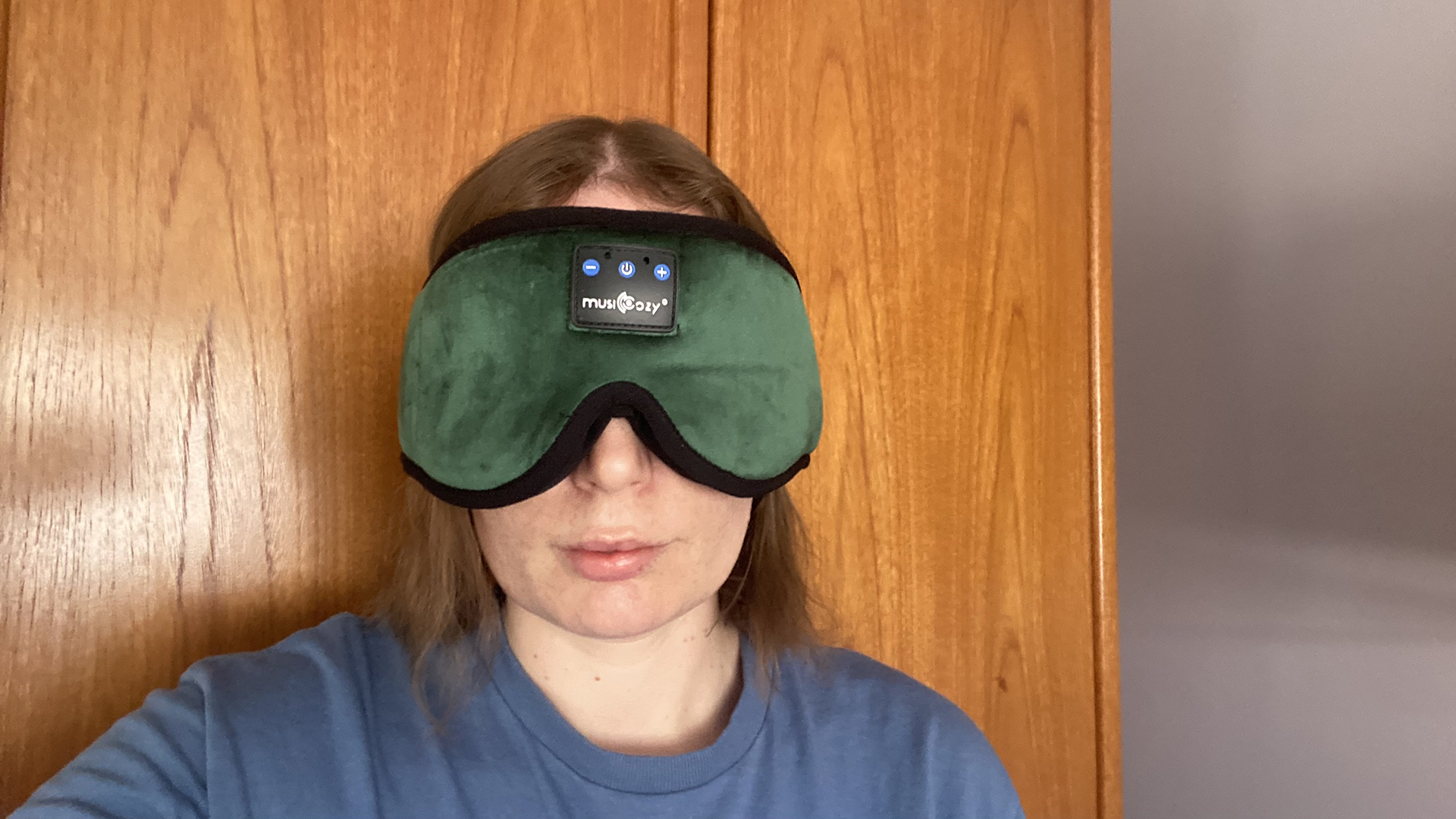 A person wearing the MUSICOZY Heaphone Sleep Mask, standing in front of a wooden door.