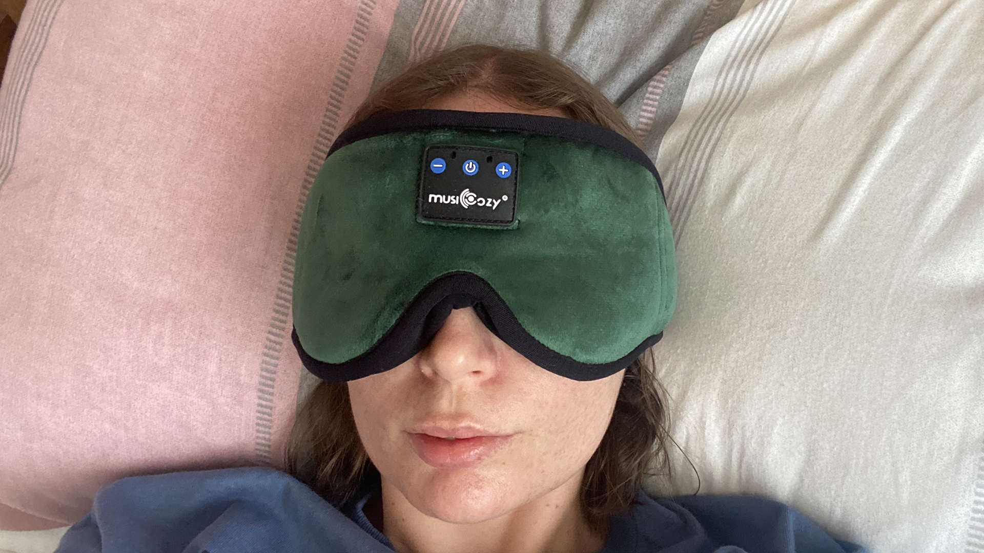 The MUSICOZY Headphone eye mask in green being worn by a member of our sleep team, as she rests against a pillow