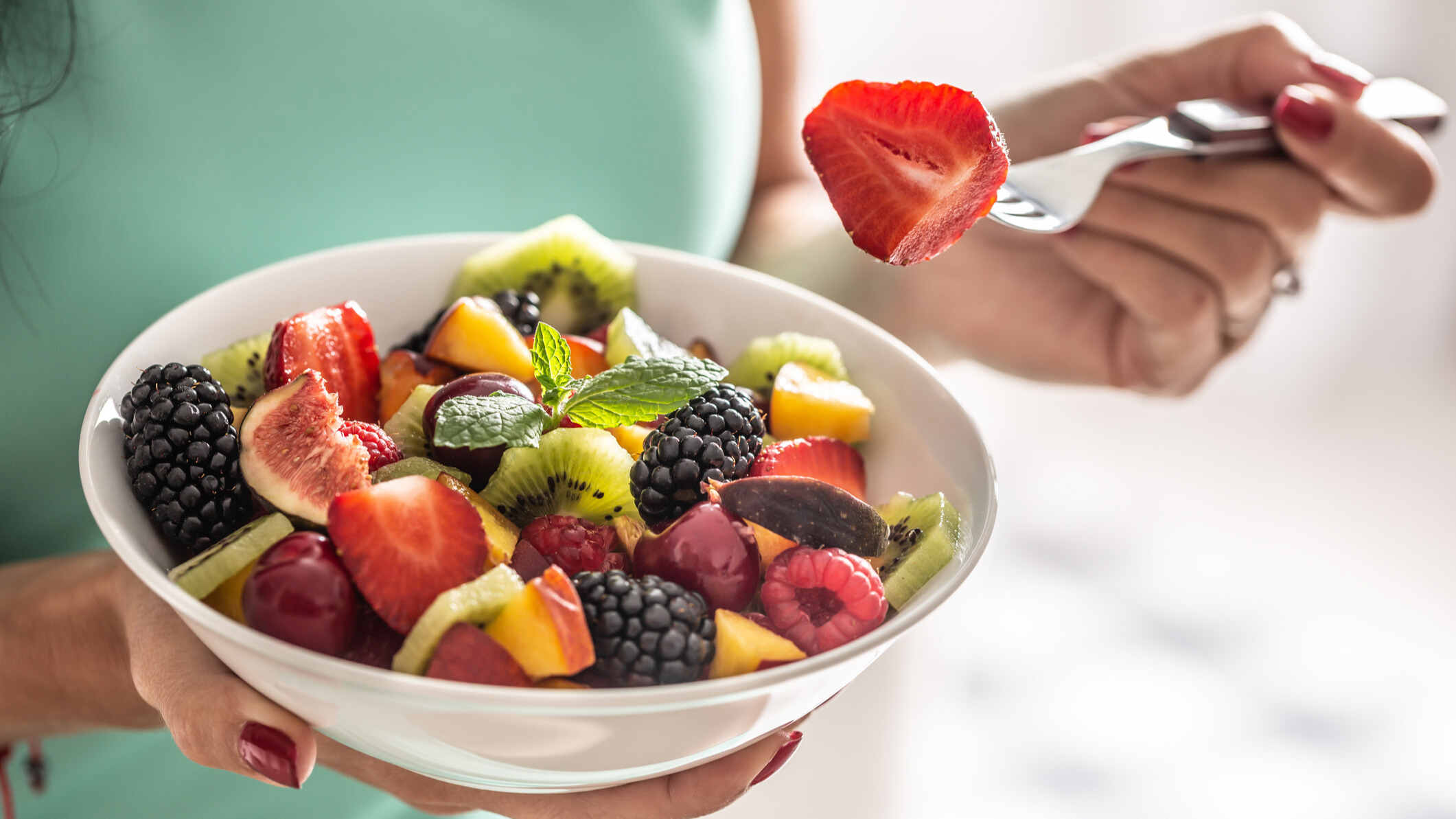 A person holding a bowl of fruits and berries