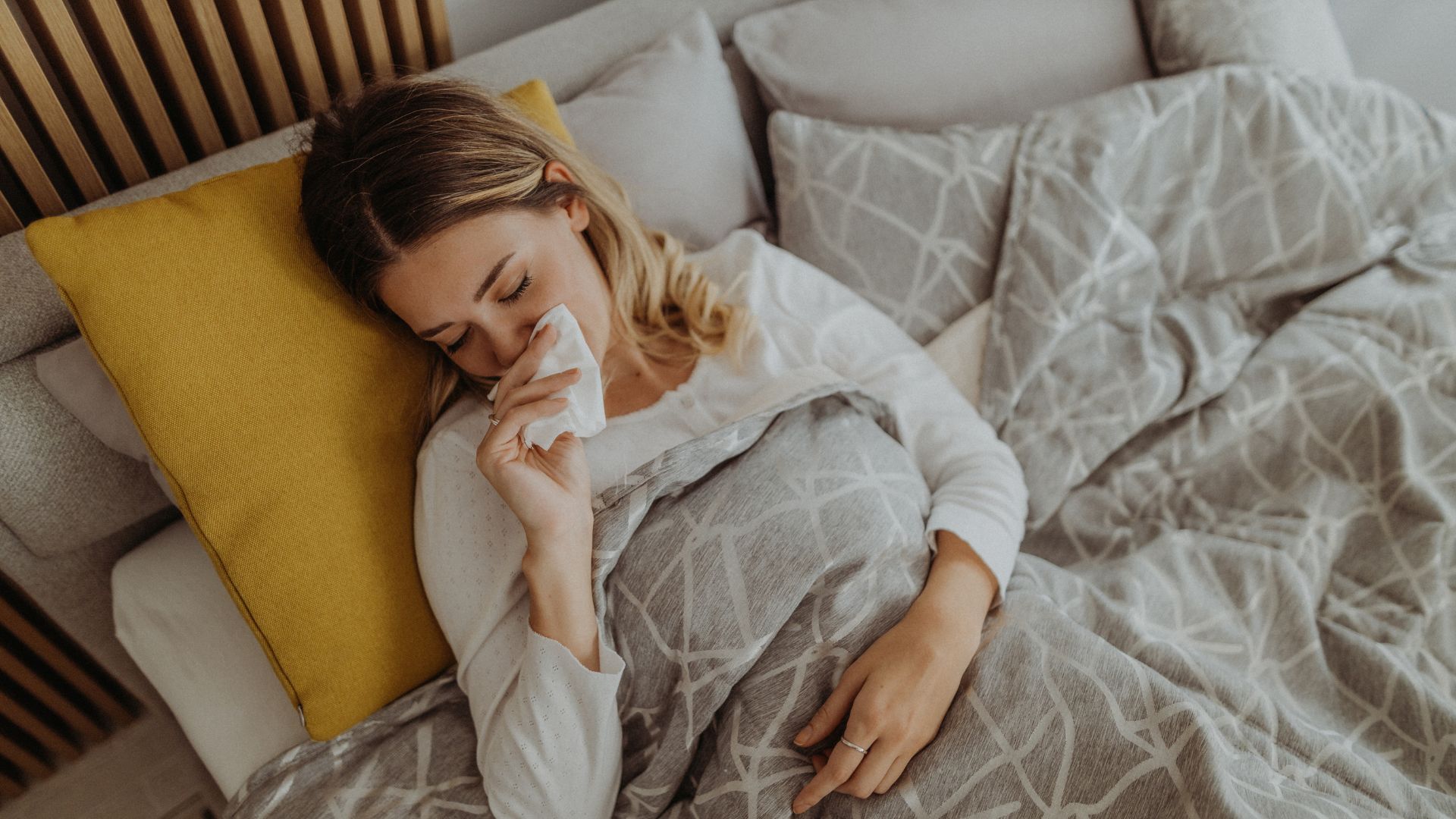 A woman with hay fever wipes stuffy nose in bed