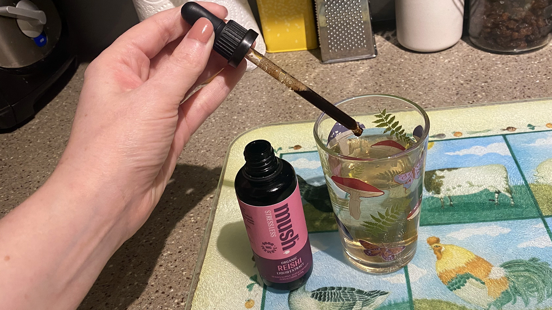 Primer plano de una mano que utiliza un cuentagotas para dispensar extracto de hongo reishi en un vaso de agua.