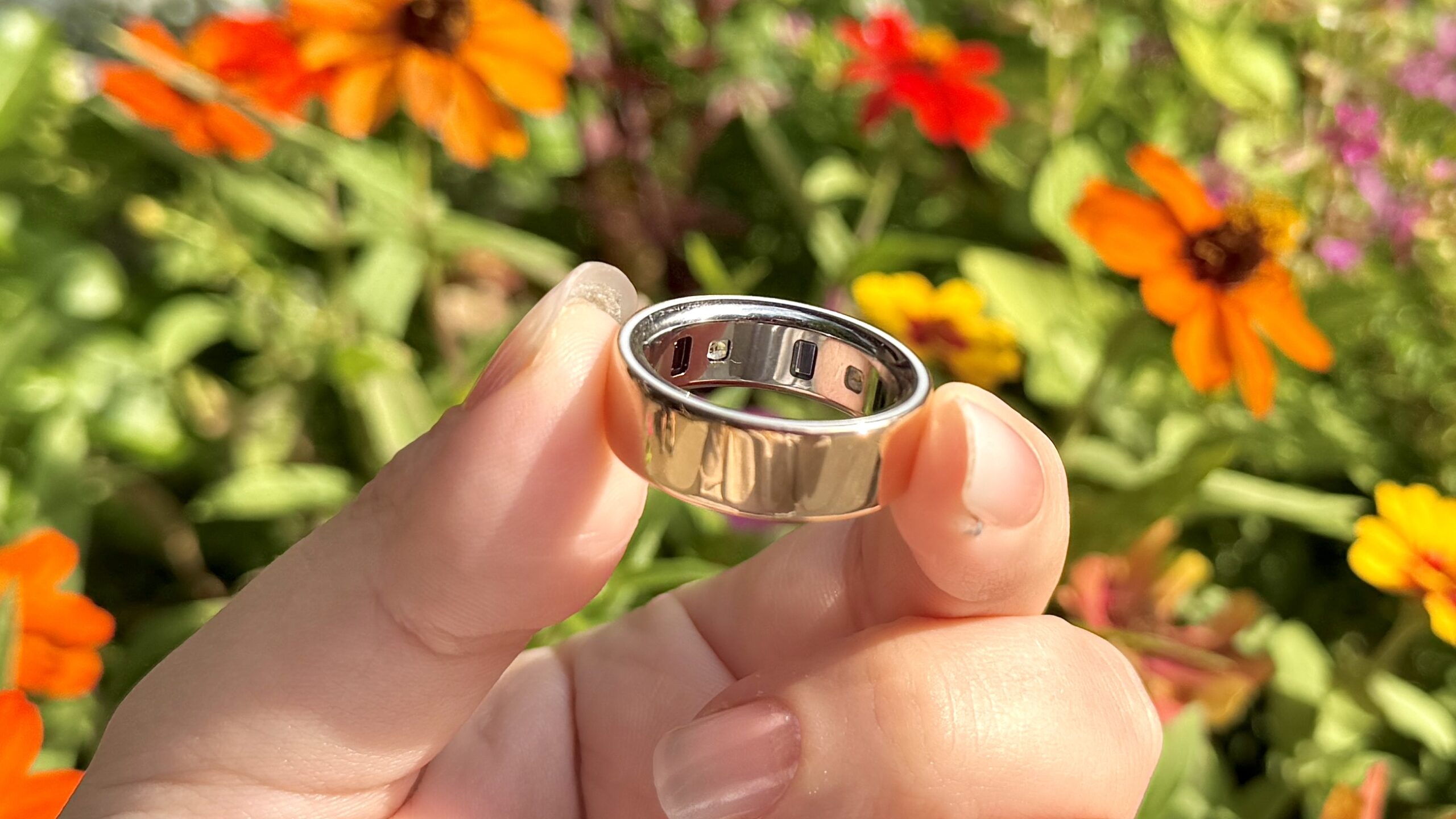 خاتم Oura Ring 4 بلون الذهب الوردي يُمسك بين أصابع شخص