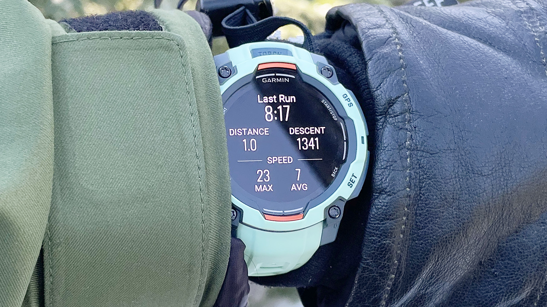 Часы Garmin Instinct 3 на запястье пользователя, крупным планом показанные между лыжной перчаткой и курткой.