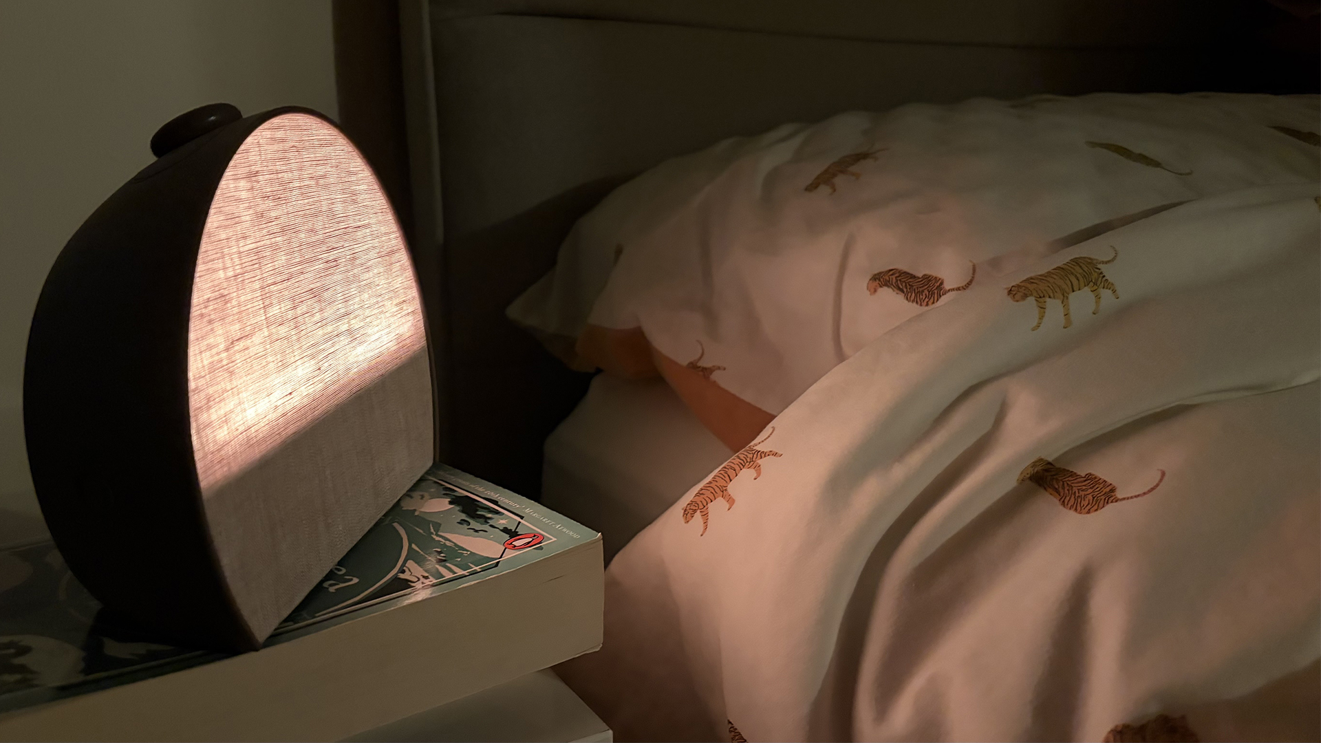 جهاز Hatch Sleep Clock يضيء بلطف باللون الأصفر بجانب سرير في غرفة مظلمة