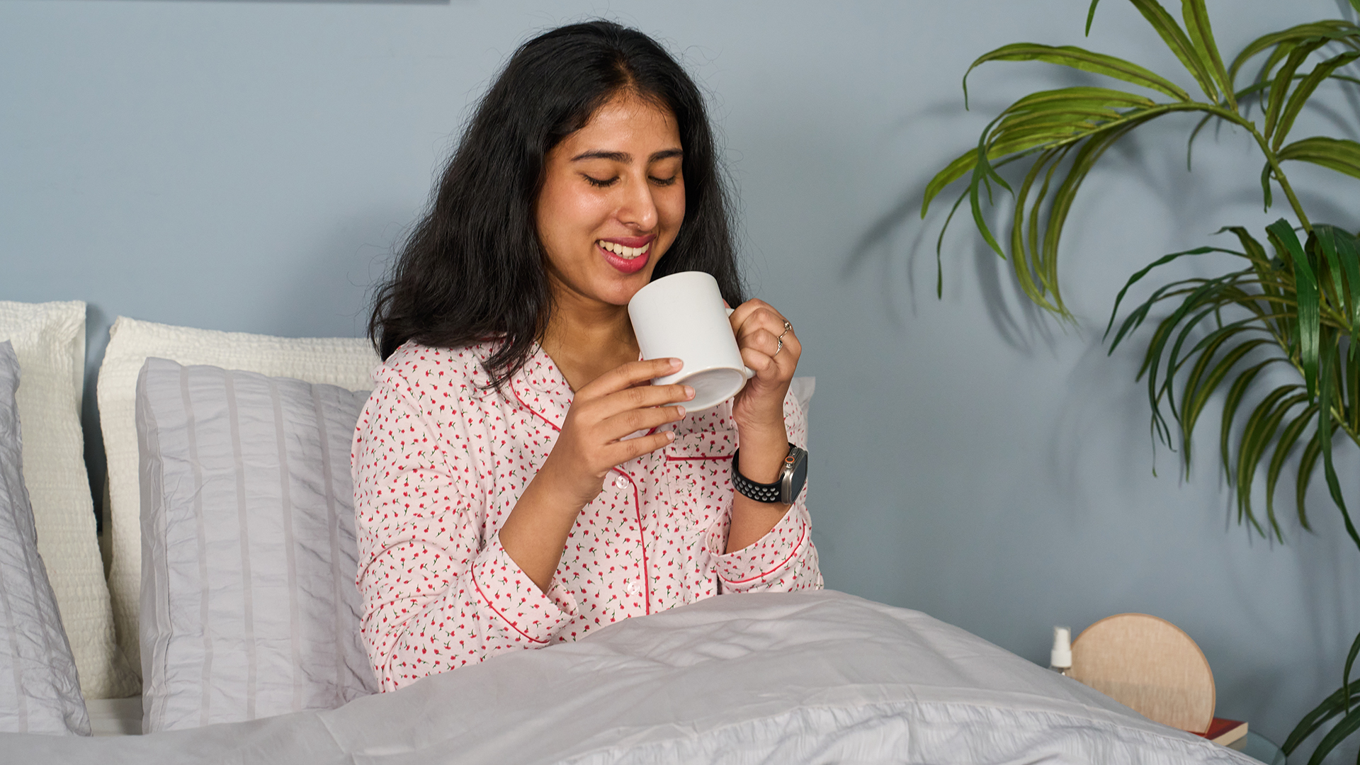Una mujer está sentada en la cama y bebe de una taza.