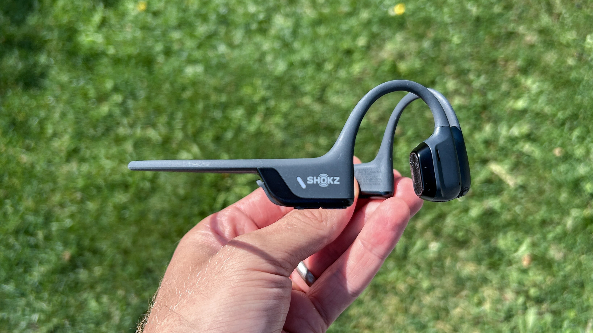 سماعات Shokz OpenRun Pro 2 في يد شخص أمام عشب