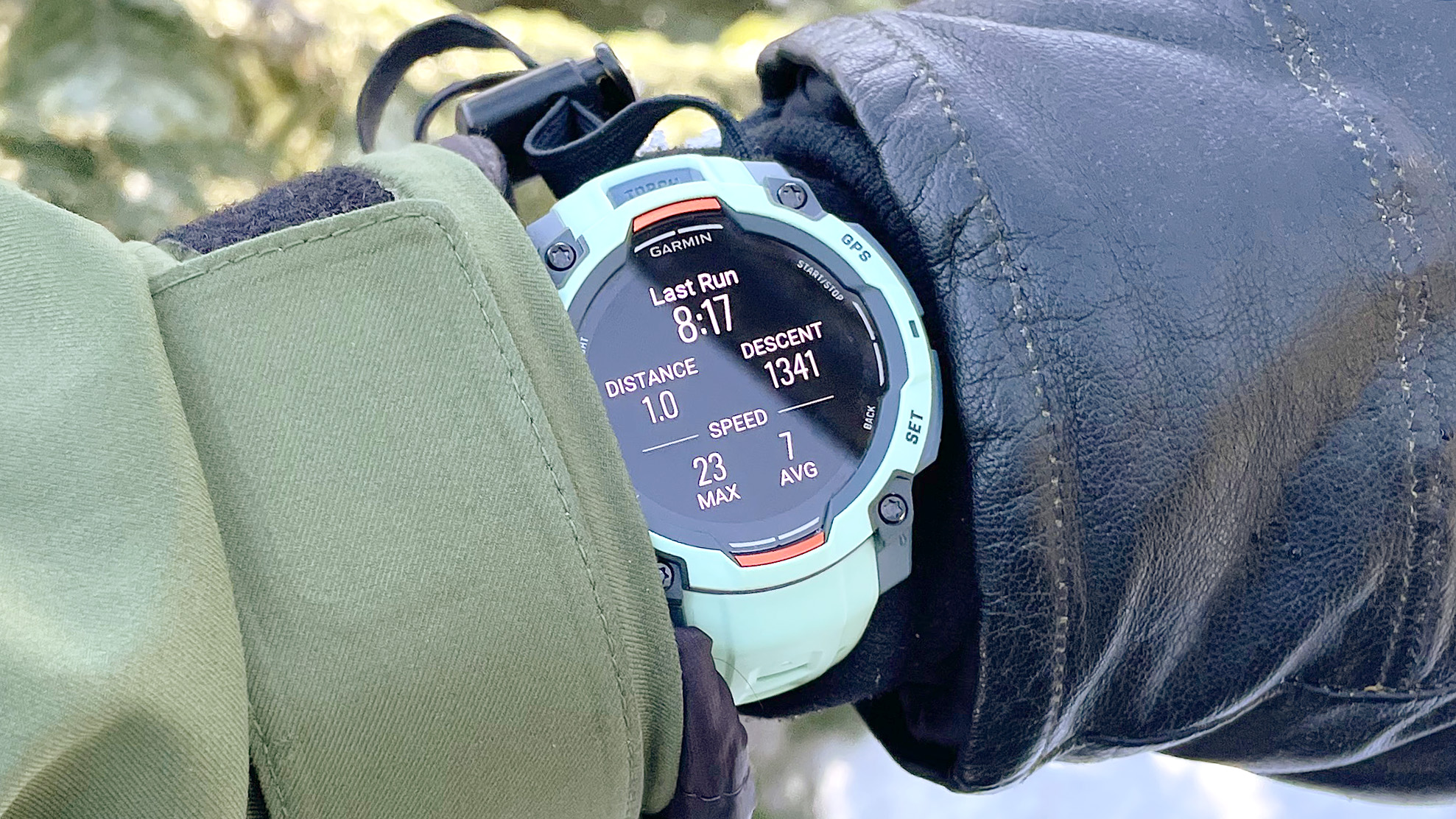 ساعة Garmin Instinct 3 على معصم المستخدم، تظهر عن قرب بين قفاز تزلج وسترة