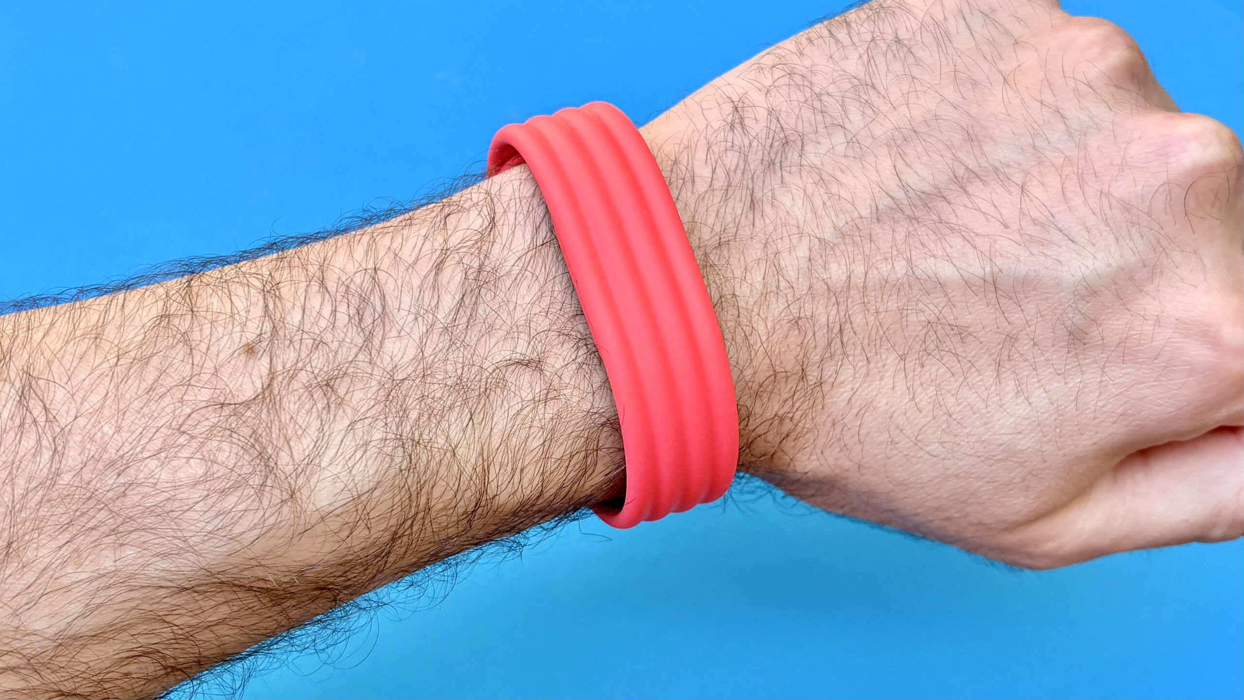 لقطة مقربة لمتتبع Fitbit Air على المعصم بحزام أحمر على خلفية زرقاء