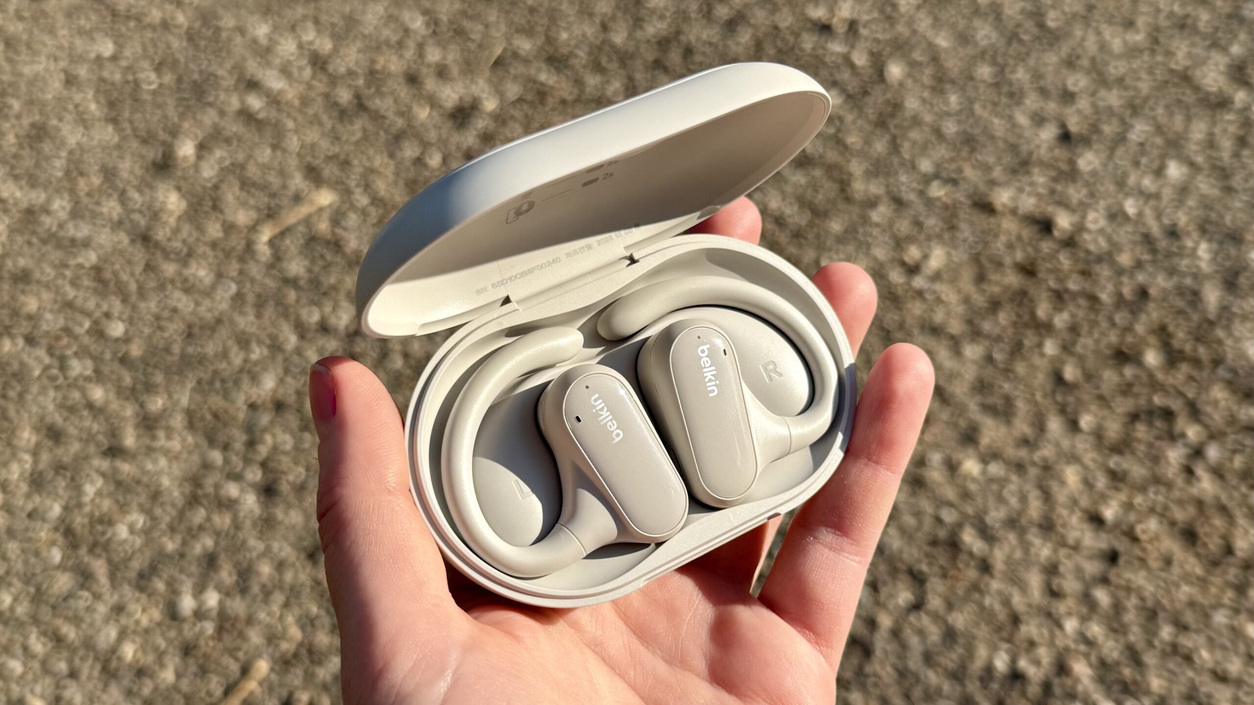 يد تحمل سماعات Belkin SoundForm ClearFit في علبة الشحن الخاصة بها.