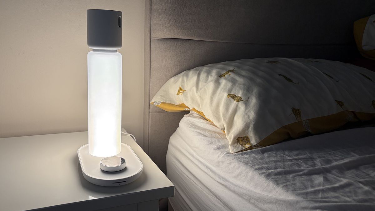 مصباح Sleepal AI في غرفة نوم مراجعنا في الظلام. المصباح مضاء، ويلقي الضوء على الوسادة.