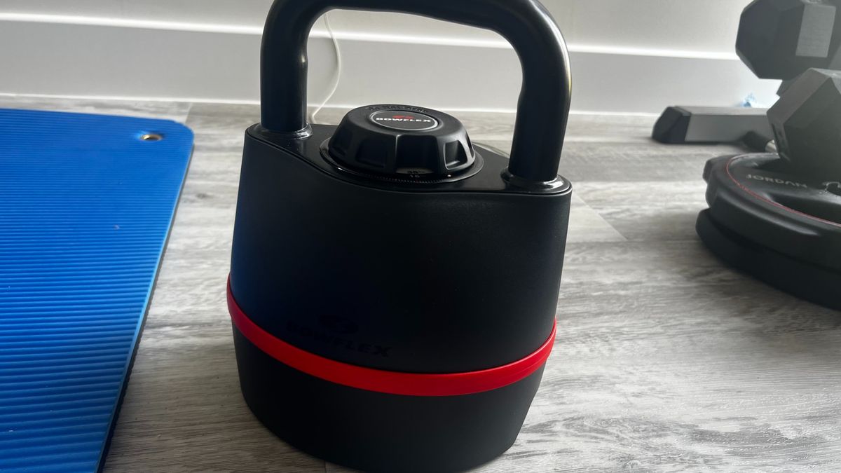 صورة لـ Bowflex SelectTech 840 kettlebell على أرضية خشبية بجانب حصيرة التمرين أثناء تدريب الكيتل بيل