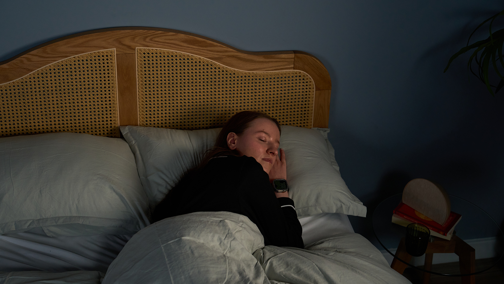Una mujer de cabello castaño largo duerme de lado sobre una almohada cómoda en una habitación azul por la noche.