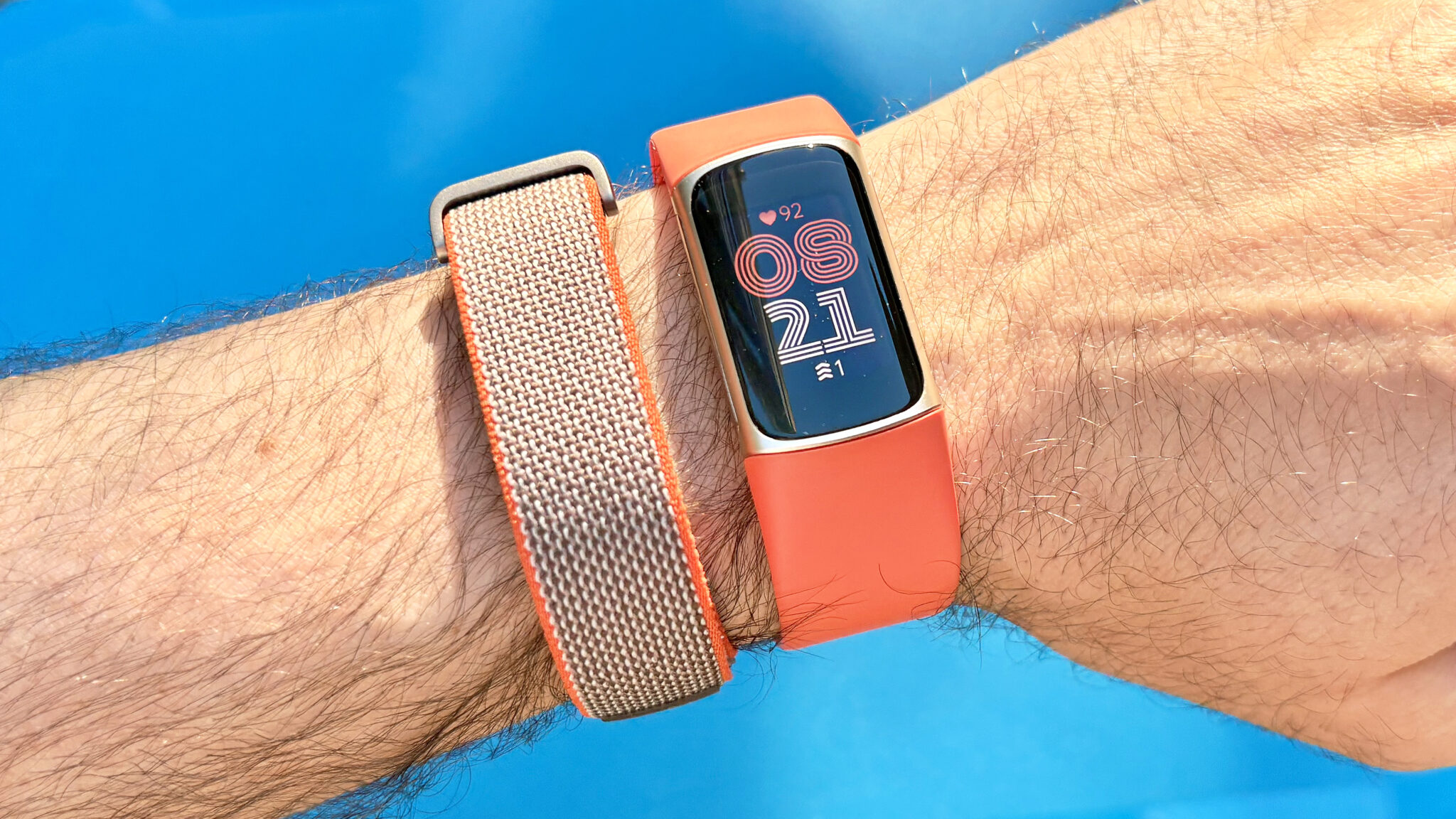 لقطة مقربة لجهازي Fitbit Air و Fitbit Charge 6 على معصم مستخدم بخلفية زرقاء